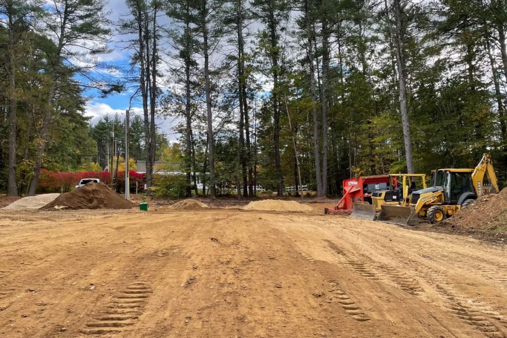 Large graded commercial lot with a backhoe and equipment staged along the treeline