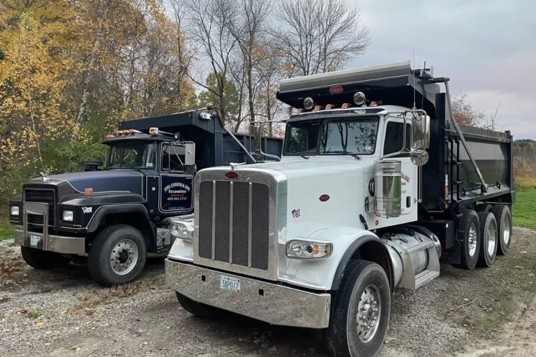 Two Joel Clough and Son dump trucks parked on a gravel yard, used for hauling loam, gravel and fill