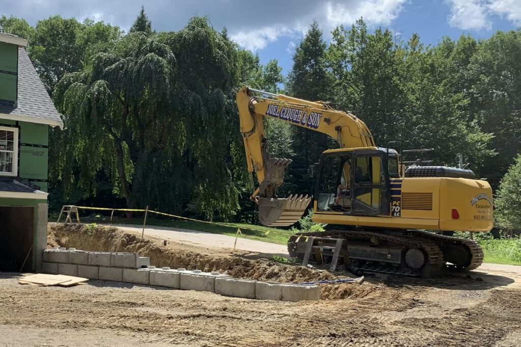 Joel Clough and Son excavator beside a new house foundation with a concrete block retaining wall being set