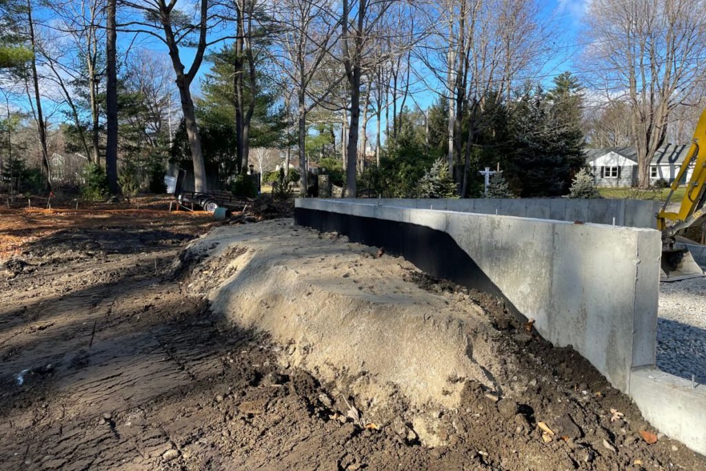 Damp-proofed concrete foundation wall with sand backfill staged alongside