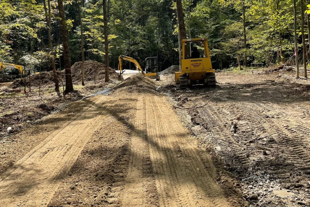 Freshly cut and graded gravel access road running through woods with a dozer and excavator working the grade
