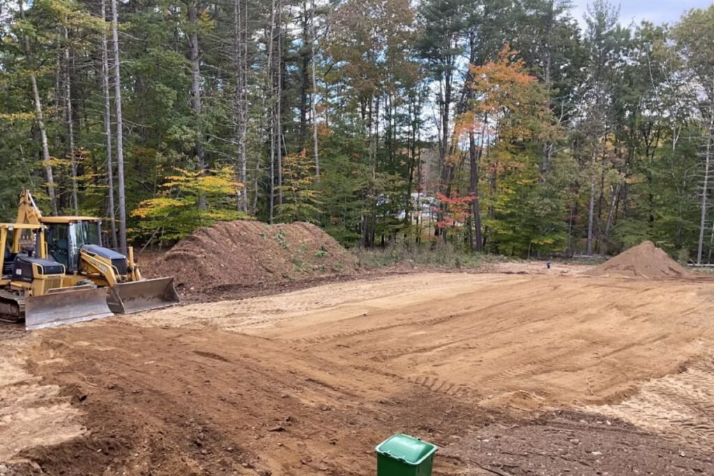 Cleared and graded house lot with a dozer working the pad and stockpiled loam alongside