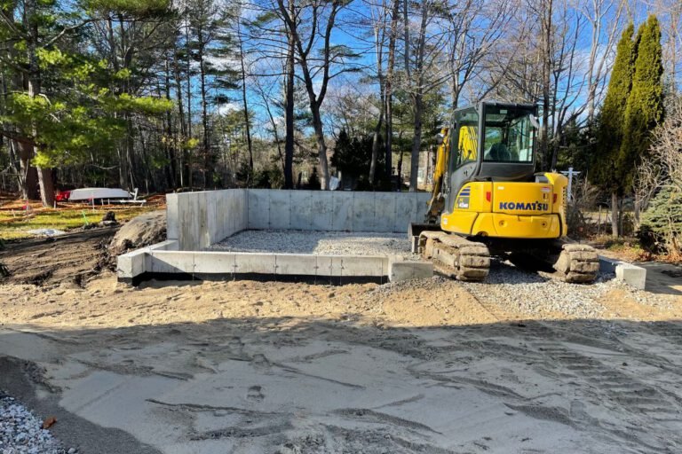 New concrete foundation and frost walls with a compacted gravel pad and excavator on a cleared lot