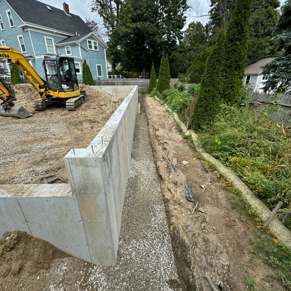 New poured concrete foundation wall with drainage stone backfill and an excavator on site