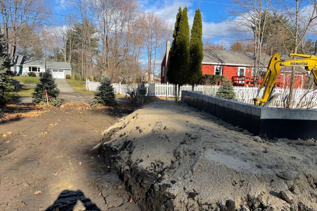 Block retaining wall built along a driveway with an excavator backfilling behind it