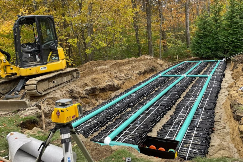 Large septic leach field with rows of chambers and green distribution piping being set to laser grade in autumn