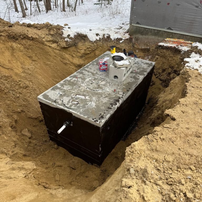 New concrete septic tank set in an open excavation with snow on the ground
