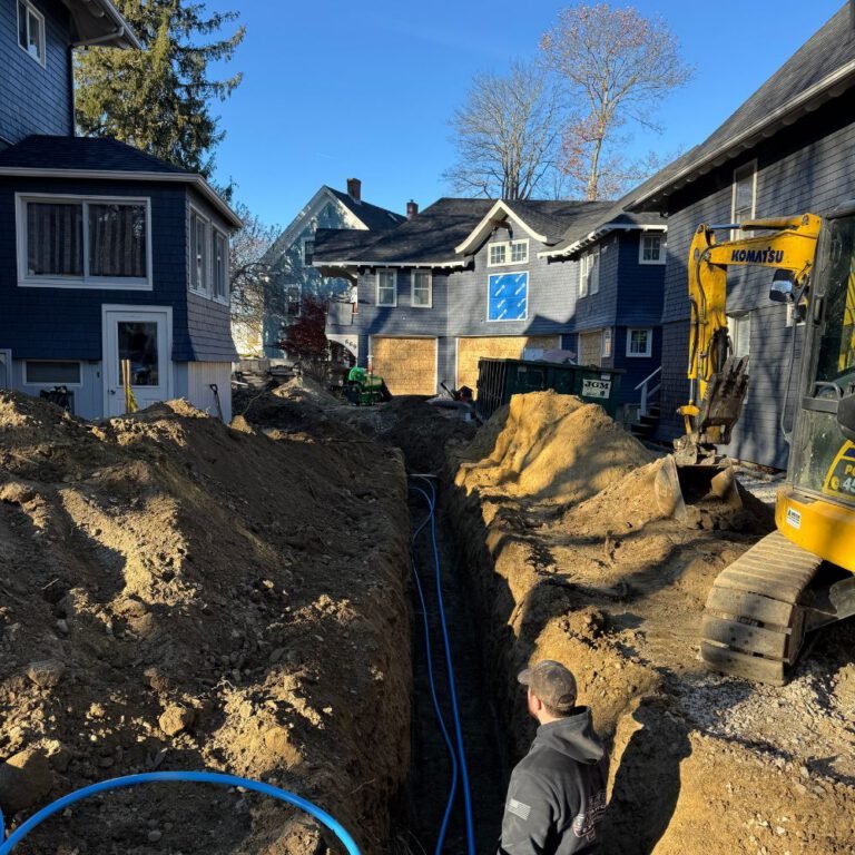 Excavator digging a water service trench between two houses with new blue service line in place