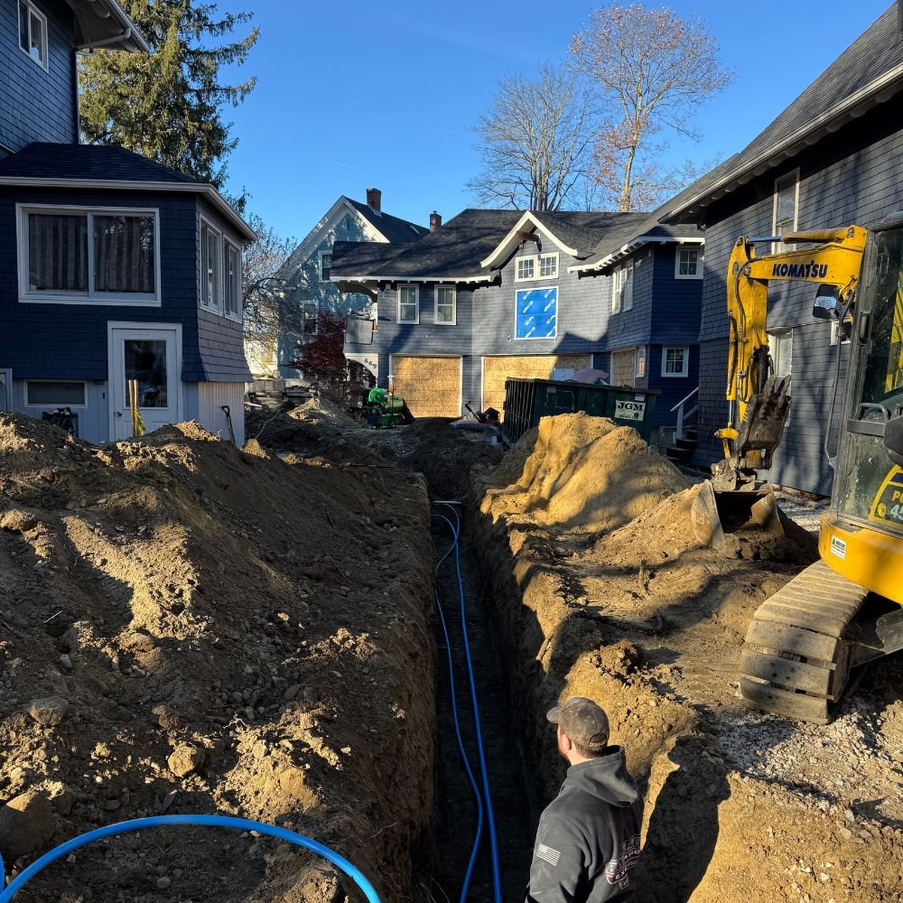 Excavator digging a water service trench between two houses with new blue service line in place